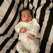 Ellias is registered to the contest to win money with this photo: baby, newborn, sleeping, white_clothing, striped_blanket, polka_dot, infant, cute, peaceful, soft, child, portrait, resting, small_hands, soft_texture, indoors, cozy, lying_down, young_child, infant_clothes
