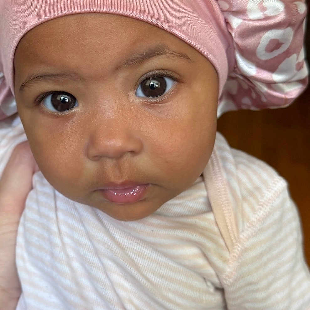 Laiani joined the competition — help win amazing prizes! baby, bonnet, child, closeup, clothing, curious, cute, expression, face, hand, headwear, indoors, infant, onesie, person, pink, portrait, skin, striped, young