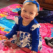 Leana participe au concours pour gagner de l'argent avec cette photo : baby, child, smiling, sitting, blue_headband, dress, floral_pattern, blanket, colorful, pacifier, socks, wooden_furniture, indoor, cute, happy, portrait, floor, playful, headband, clothing