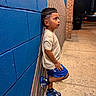 child, boy, toddler, portrait, profile, outdoor, night, street, sidewalk, brick_wall, blue_wall, mural, standing, balancing, fashion, haircut, sneakers, shorts, t_shirt, urban