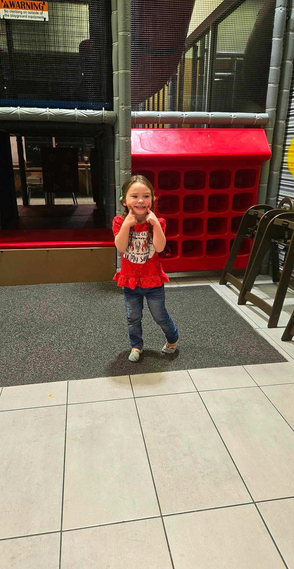 Allayna joined the competition — help win amazing prizes! child, girl, smiling, red_shirt, jeans, indoor, playground, play_equipment, netting, floor_tiles, happy, posing, casual_clothing, young, cute, fun, childhood, play_area, colorful, joyful