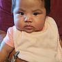 baby, child, infant, face, chubby_cheeks, bib, pink_clothing, arm, hand, wooden_chair, person, indoor, portrait, holding, seated, short_hair, serious_expression, skin, clothing, fabric