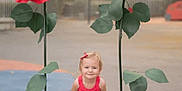 Léa a rejoint le concours — aidez-le/la à gagner de superbes lots ! child, girl, red_dress, smiling, outdoor, large_flowers, artificial_flowers, playground, summer, green_leaves, standing, cute, happy, sandals, nature, fun, posing, daylight, park, background_blur
