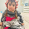 child, toddler, portrait, sitting, bedroom, bed, blanket, bonnet, braids, gray_sweater, pink_clothing, dress, leopard_print, wide_eyed, serious_expression, indoors, furniture, mirror, dresser, home