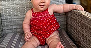 Kamryn joined the competition — help win amazing prizes! baby, bow, casual, child, chubby_legs, comfortable, curious, cute, headband, indoors, infant, person, portrait, red_clothing, romper, sitting, smiling, striped_cushion, wicker_chair, young_child