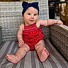 baby, child, infant, headband, bow, red_clothing, romper, wicker_chair, striped_cushion, sitting, cute, smiling, indoors, portrait, chubby_legs, curious, person, young_child, comfortable, casual