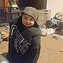 toddler, child, hoodie, cap, smile, indoor, carpet, toy, footwear, furniture, television, cabinet, playpen, stuffed_toy, keys, messy_room, person, clothing, barefoot, home