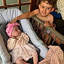 baby, child, infant, boy, smiling, indoor, baby_seat, pink_headband, pink_dress, blanket, furniture, door, couch, happy, face, portrait, sibling, toddler, hand, person
