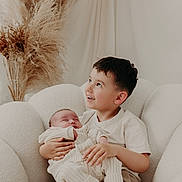 Jack participe au concours pour gagner de l'argent avec cette photo : child, baby, holding, smiling, sitting, chair, cozy, indoor, family, love, happiness, pampas_grass, neutral_colors, soft_lighting, portrait, candid, toddler, infant, clothing, relaxation