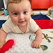 Sacha a rejoint le concours — aidez-le/la à gagner de superbes lots ! baby, smiling, face, infant, toy, pacifier, play_mat, indoor, floor, clothing, hand, colorful, soft_toy, wood_floor, furniture, child, cute, happy, portrait, toddler