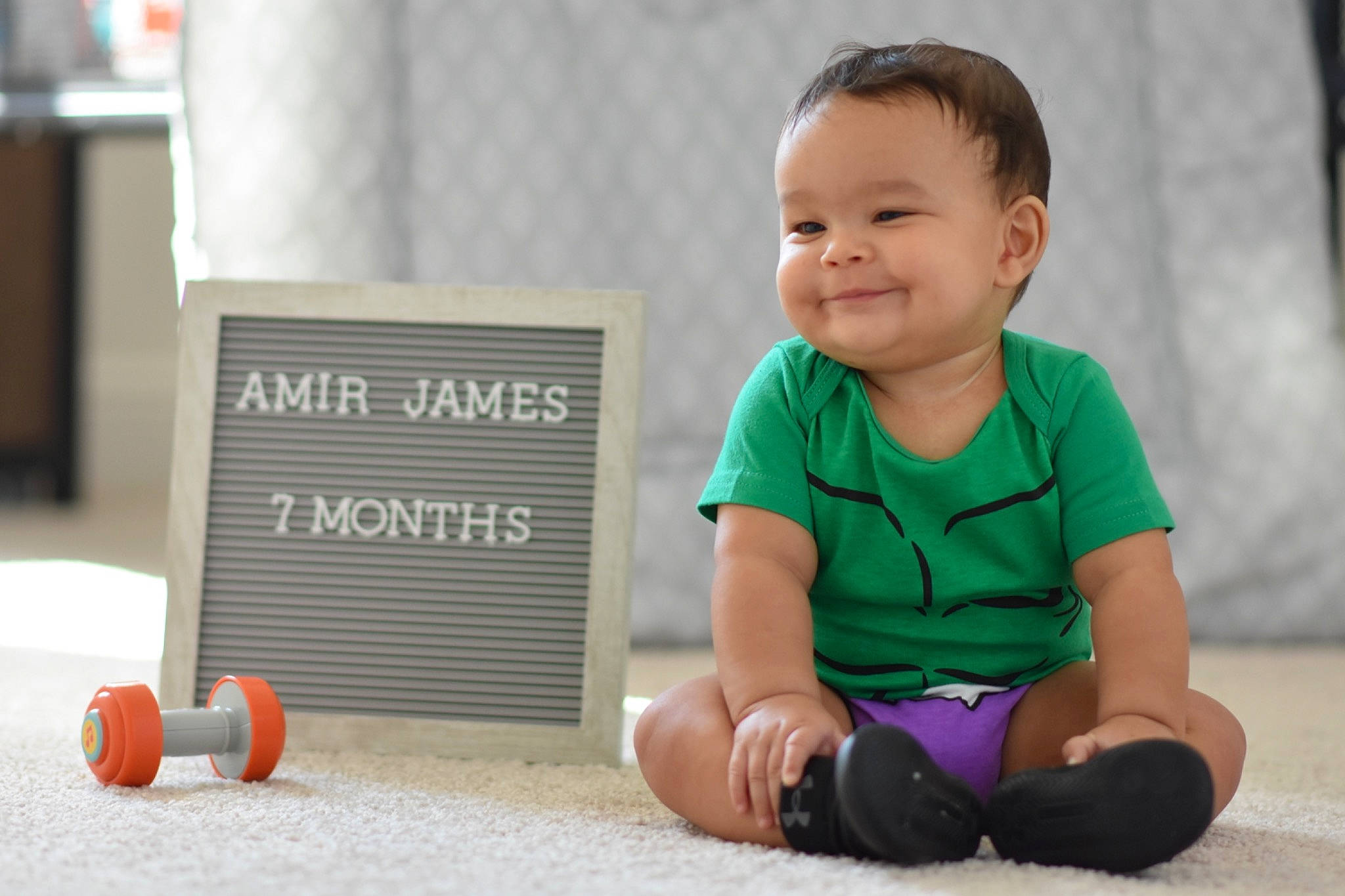 Amir is registered to the contest to win money with this photo: baby, baby_playing_with_toys, baby_toddler_clothing, child, face, floor, flooring, fun, grass, happy, joy, knee, leisure, person, sitting, skin, sleeve, smile, sock, t_shirt