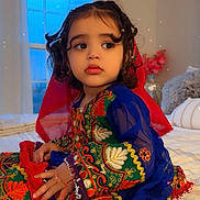 Ayat joined the competition — help win amazing prizes! toddler, child, traditional_clothing, embroidered_outfit, blue_sleeves, red_scarf, bedroom, window, curtains, bedspread, indoor, portrait, sitting, curly_hair, bracelet, decor, soft_light, sparkles, serene, cute