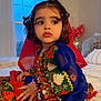 toddler, child, traditional_clothing, embroidered_outfit, blue_sleeves, red_scarf, bedroom, window, curtains, bedspread, indoor, portrait, sitting, curly_hair, bracelet, decor, soft_light, sparkles, serene, cute