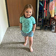 Aurora is registered to the contest to win money with this photo: toddler, child, barefoot, carpet, door, shorts, shirt, smiling, standing, indoor, clothing, shoe_organizer, wood, hand_in_pocket, person, young_child, home, casual, feet, happy