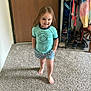 toddler, child, barefoot, carpet, door, shorts, shirt, smiling, standing, indoor, clothing, shoe_organizer, wood, hand_in_pocket, person, young_child, home, casual, feet, happy