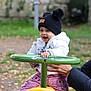toddler, child, playground, toy, green_handlebar, yellow_toy, autumn_leaves, outdoor, smiling, white_jacket, black_hat, pom_poms, hand_support, pink_pants, daisy_duck, happy, person, park, fall, cute