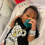 Ace is registered to the contest to win money with this photo: baby, newborn, pacifier, hospital, crib, onesie, bear_print, necklace, gold, bracelet, infant, cute, sleeping, hand, face, person, indoors, blanket, clothing, bed