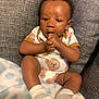 baby, infant, child, onesie, bear_pattern, hand_in_mouth, socks, blanket, couch, seated, curious, soft_lighting, indoors, cute, portrait, cozy, young_child, skin, expression, comfortable