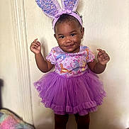 Ariel is registered to the contest to win money with this photo: toddler, child, smiling, purple_tutu, bunny_ears, indoor, cute, happy, standing, clothing, shoes, headband, playful, portrait, person, fashion, fun, expressive, young_child, adorable