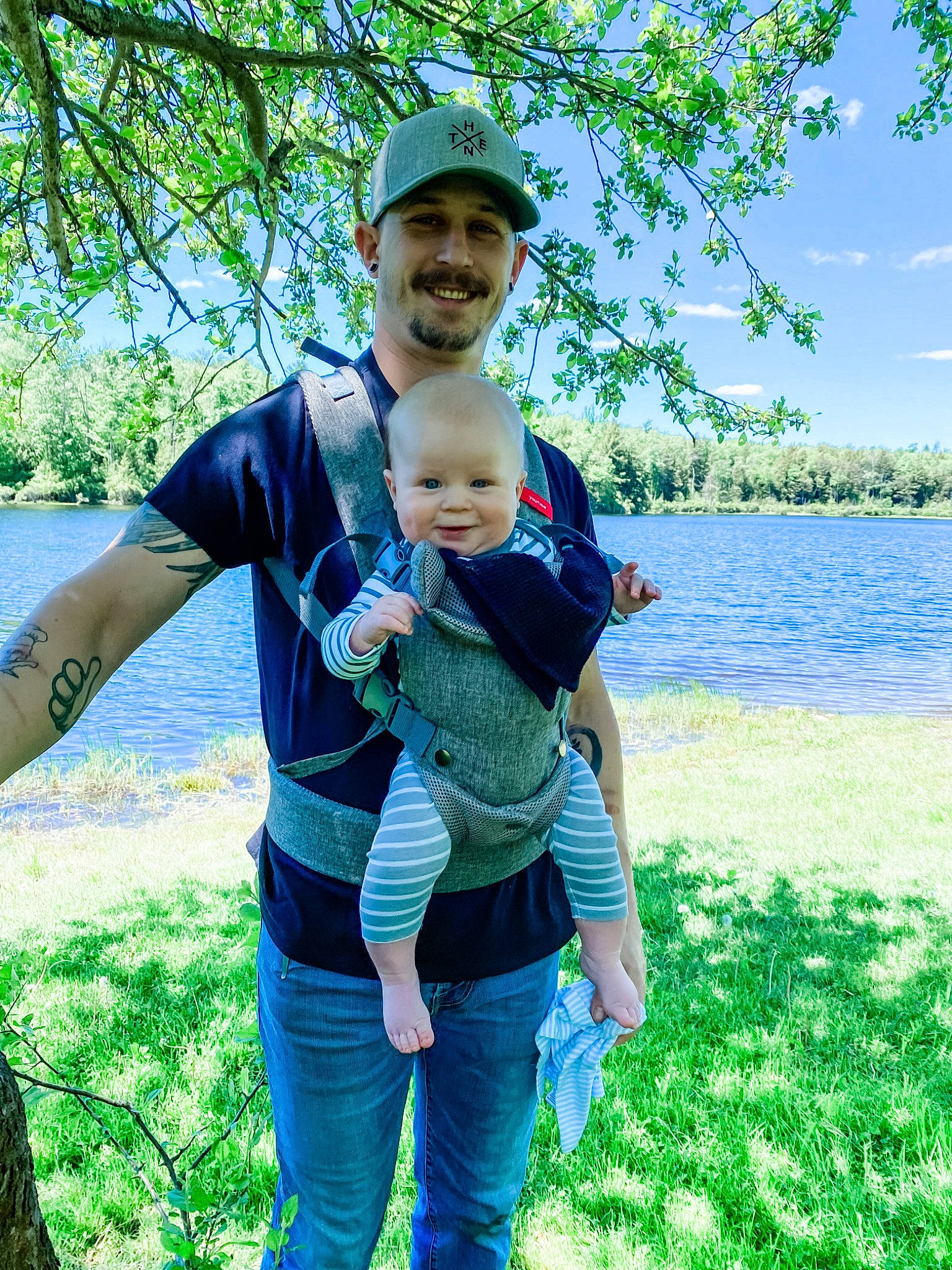Lee is registered to the contest to win money with this photo: azure, botany, fedora, fun, grass, green, happy, hat, headwear, jeans, joy, lake, leisure, nature, people_in_nature, person, plant, sky, smile, sun_hat