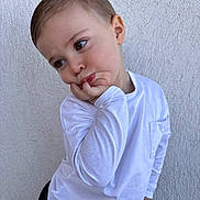 Diego a rejoint le concours — aidez-le/la à gagner de superbes lots ! child, toddler, boy, portrait, white_shirt, hand_on_face, pensive, cute, short_hair, brown_eyes, long_eyelashes, textured_wall, stucco_wall, leaning, casual_clothing, skin, ear, expression, closeup, photography