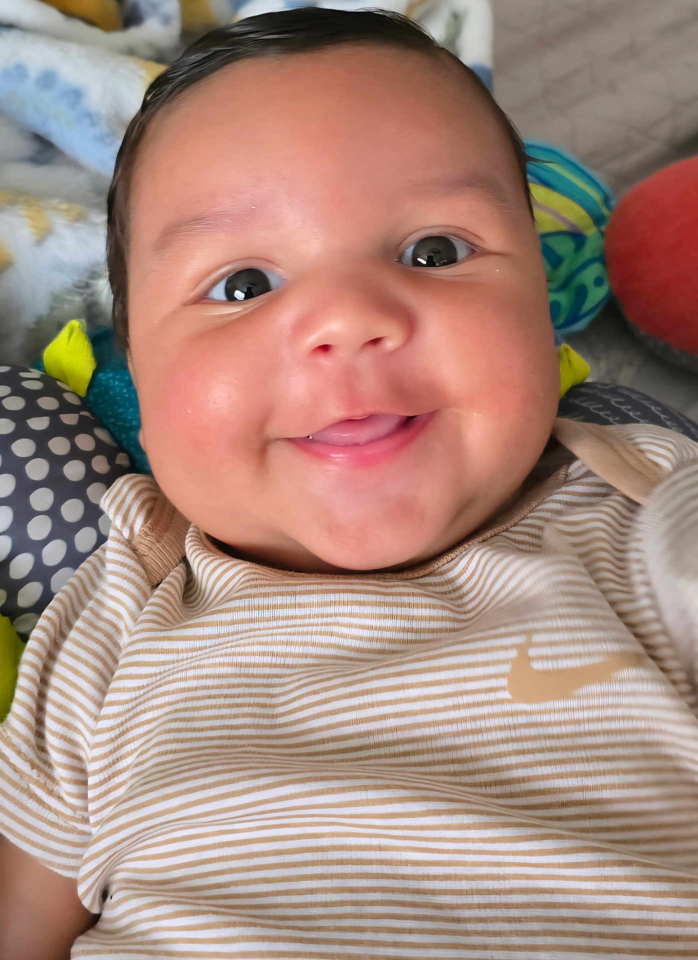 Miles is registered to the contest to win money with this photo: baby, child, smiling, face, closeup, striped_shirt, toy, blanket, happy, infant, cute, indoors, portrait, skin, head, person, clothing, soft_toy, eyes, cheeks