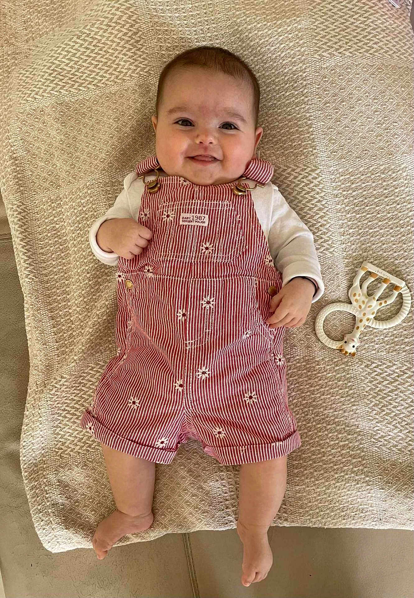 Marla a rejoint le concours — aidez-le/la à gagner de superbes lots ! baby, smiling, overalls, striped_clothing, toy, giraffe_toy, blanket, floor, happy, infant, cute, child, laying_down, teething_toy, patterned_clothing, indoors, person, small_child, playtime, expression