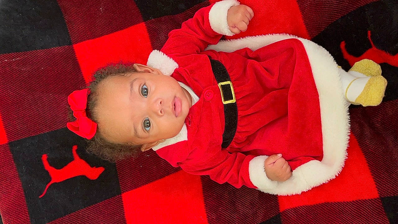 Amoura is registered to the contest to win money with this photo: baby, baby_toddler_clothing, carmine, child, christmas, christmas_eve, comfort, event, fictional_character, flooring, fun, hat, head, holiday, lap, pattern, person, red, sleeve, smile