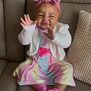 Aaliyah is registered to the contest to win money with this photo: baby, child, smiling, happy, sitting, couch, headband, pink, dress, cardigan, socks, hands, waving, indoor, cute, infant, colorful, striped, furniture, portrait
