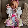 baby, child, smiling, happy, sitting, couch, headband, pink, dress, cardigan, socks, hands, waving, indoor, cute, infant, colorful, striped, furniture, portrait