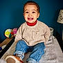 toddler, child, smiling, sweater, jeans, slippers, indoor, blanket, lamp, toy, colorful_ball, happy, portrait, casual_clothing, cozy, furniture, home, young_child, seated, cute