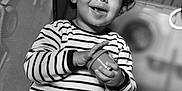 Nevan participe au concours pour gagner de l'argent avec cette photo : toddler, child, curly_hair, striped_clothing, onesie, smiling, happy, indoor, playpen, baby_toy, black_and_white, portrait, seated, infant, cute, small_hands, face, eyes, expression, young_child