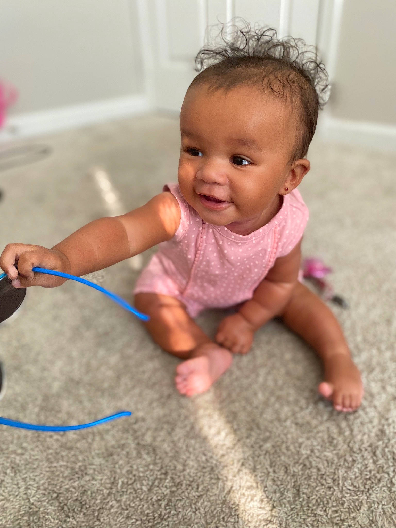 Joni is registered to the contest to win money with this photo: baby, baby_toddler_clothing, cheek, child, facial_expression, finger, floor, flooring, fun, happy, hardwood, human_leg, joint, person, pink, skin, smile, standing, thumb, toddler
