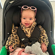 Lucia joined the competition — help win amazing prizes! baby, child, car_seat, fuzzy_jacket, leopard_print, pink_sunglasses, stuffed_animal, elephant_toy, blanket, indoor, smiling, happy, person, cute, cozy, infant, seatbelt, clothing, portrait, young_child