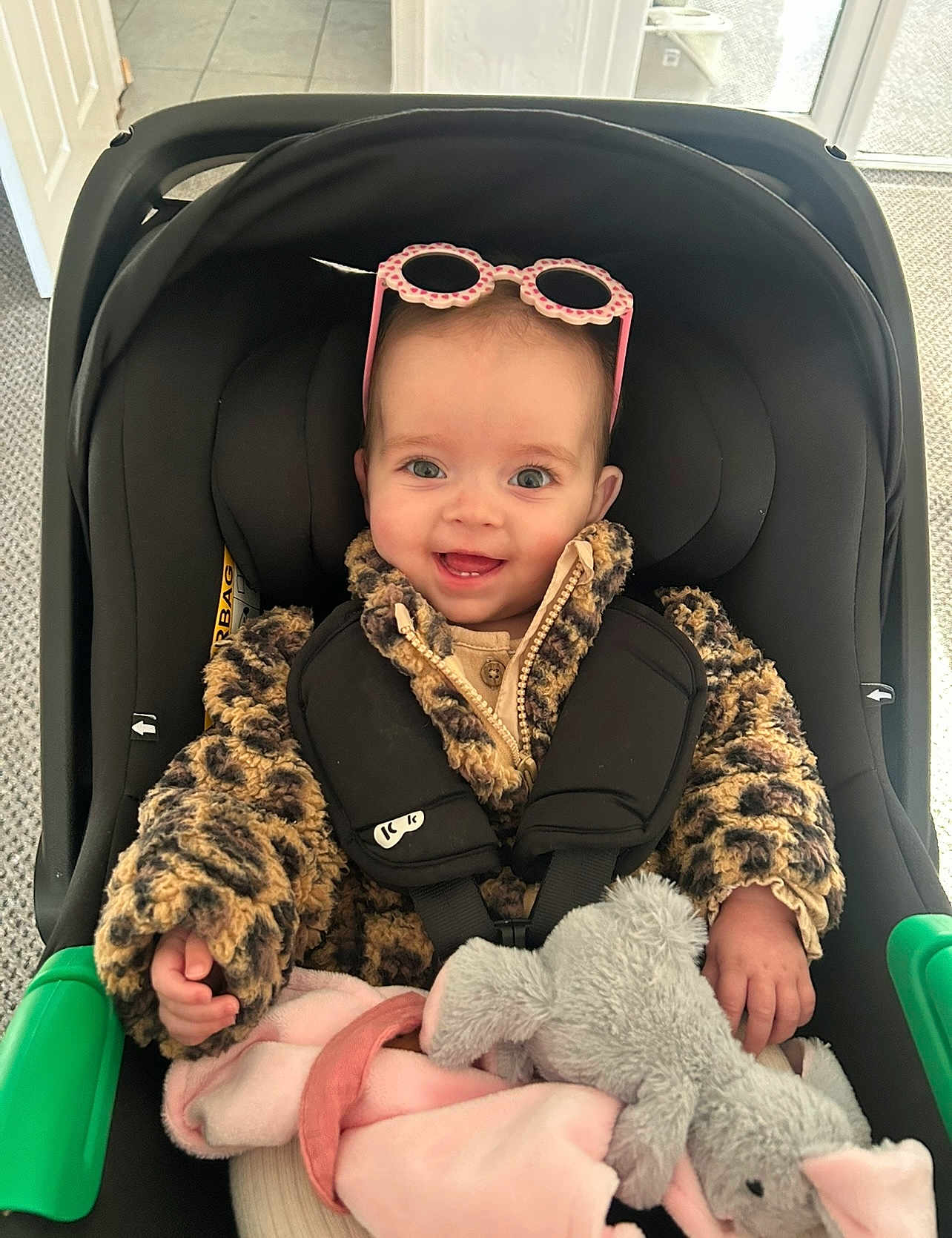 Lucia joined the competition — help win amazing prizes! baby, child, car_seat, fuzzy_jacket, leopard_print, pink_sunglasses, stuffed_animal, elephant_toy, blanket, indoor, smiling, happy, person, cute, cozy, infant, seatbelt, clothing, portrait, young_child