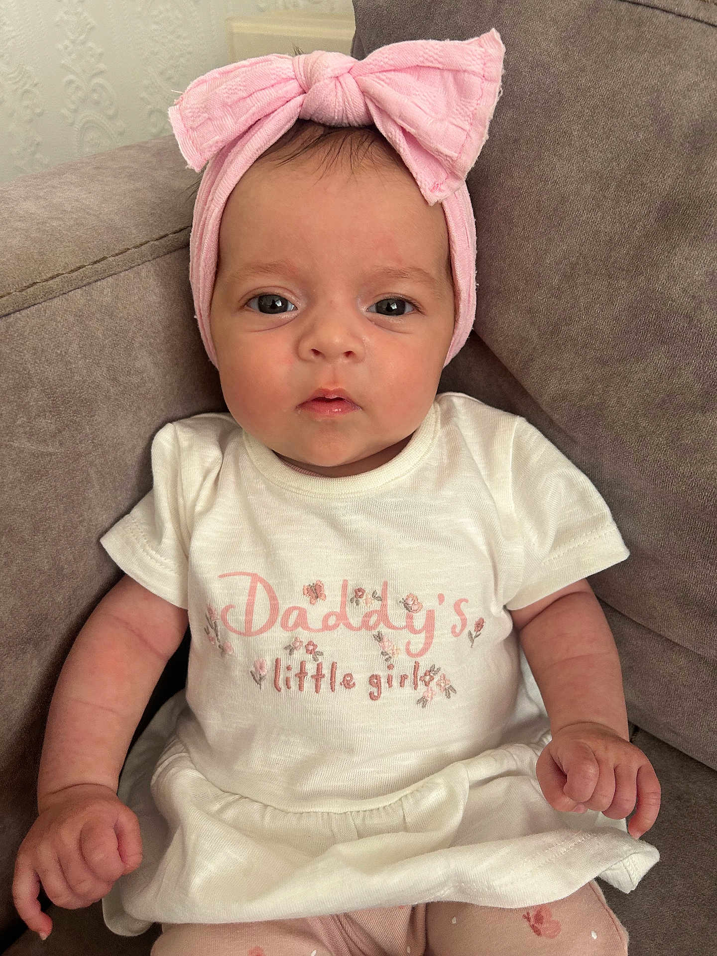 Lucia is registered to the contest to win money with this photo: baby, child, girl, pink_bow, headband, white_dress, sitting, couch, indoor, cute, portrait, closeup, young_child, clothing, hand, face, eyes, expression, soft_fabric, comfortable