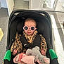 baby, sunglasses, leopard_print, car_seat, plush_toy, blanket, indoor, carpet, door, sunlight, child, cute, fashion, toddler, smile, clothing, person, toy, seatbelt, home