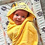 baby, towel, yellow, smile, face, hood, animal_design, floral_pattern, changing_pad, cute, child, wrapped, soft_texture, indoor, person, infant, happy, lying_down, closeup, adorable