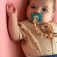 Layla is registered to the contest to win money with this photo: baby, pacifier, infant, pink_background, floral_onesie, blue_pants, hand, face, eyes, skin, clothing, cute, lying_down, child, portrait, indoor, soft_lighting, expression, closeup, adorable