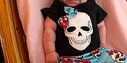 Layla joined the competition — help win amazing prizes! baby, infant, smiling, skull_print, clothing, blue_pants, floral_pattern, bow, pink_blanket, wooden_cradle, cute, happy, child, portrait, indoors, person, laying_down, small_feet, chubby_arms, cozy