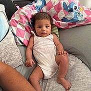 Freya is registered to the contest to win money with this photo: baby, infant, child, white_outfit, cushion, blanket, stitch_character, soft_furniture, indoor, person, skin, face, arm, leg, cute, relaxed, looking_at_camera, comfort, home, casual