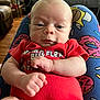 Cashton joined the competition — help win amazing prizes! baby, infant, red_onesie, face, hands, clenched_fists, blanket, donut_pattern, indoor, furniture, couch, plant, wood_floor, expression, curious, person, portrait, close_up, head, skin