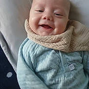 Zander is registered to the contest to win money with this photo: baby, smiling, infant, blue_clothing, bib, bed, blanket, cozy, face, head, closeup, happy, child, person, indoors, soft_texture, cute, young, portrait, resting