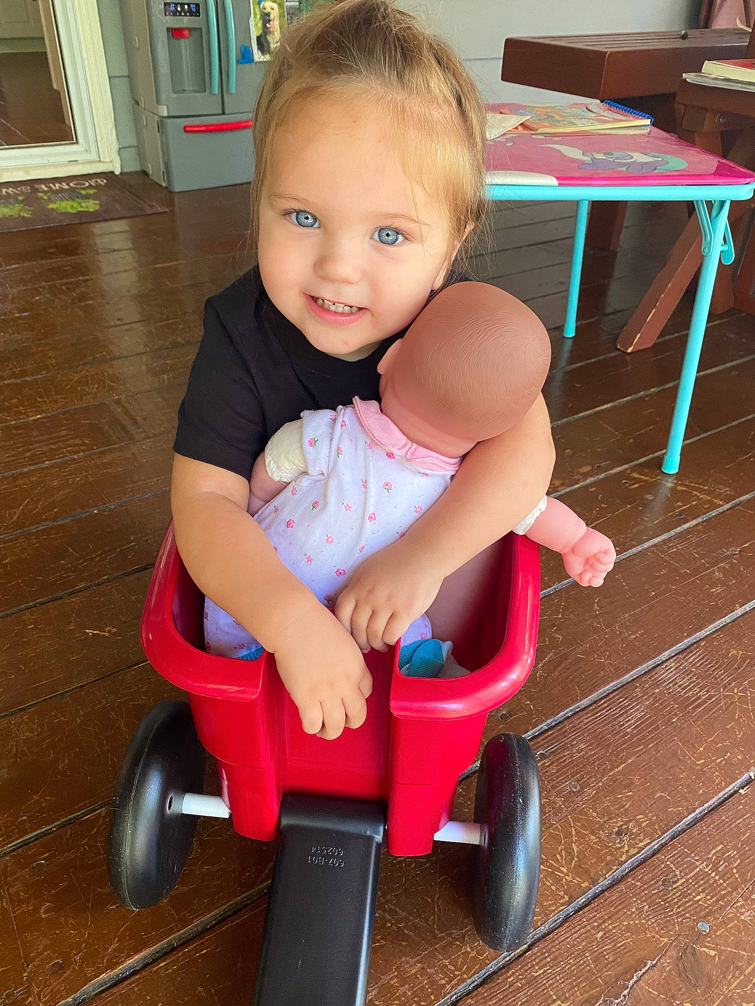 Sloane is registered to the contest to win money with this photo: automotive_wheel_system, baby, baby_toddler_clothing, child, electric_blue, flooring, fun, happy, hardwood, joy, person, play, riding_toy, rolling, sitting, smile, table, tire, toddler, vehicle