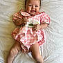 baby, infant, smile, pink_dress, checkered_pattern, lying_down, white_sheet, happy, cute, child, skin, face, hands, legs, toes, short_hair, indoors, portrait, one_person, young_child