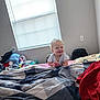 Kaizen is registered to the contest to win money with this photo: baby, child, bed, blanket, curly_hair, indoor, window, blinds, laundry, pile, clothing, smile, cheeky, person, room, fabric, diaper, red_cloth, plaid_pattern, light