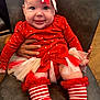 baby, child, smiling, red_clothing, headband, bow, striped_socks, tulle_skirt, hand, chair, indoor, person, happy, festive, cute, toddler, face, sitting, closeup, holiday