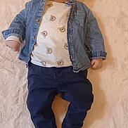 émile a rejoint le concours — aidez-le/la à gagner de superbes lots ! baby, infant, denim_jacket, bear_pattern, white_rug, blue_pants, socks, floor, smile, lying_down, child, cute, casual_clothing, indoor, portrait, young_child, happy, person, soft_texture, comfortable