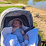 baby, sleeping, stroller, blanket, outdoor, lake, water, grass, trees, sunlight, nature, park, infant, peaceful, relaxing, scenic, bridge, daytime, clothing, comfort