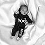 baby, infant, child, black_clothing, hoodie, pants, polka_dot_socks, blanket, white_background, soft_texture, lying_down, portrait, cute, expression, small_fist, looking_away, comfortable, indoors, monochrome, casual_wear